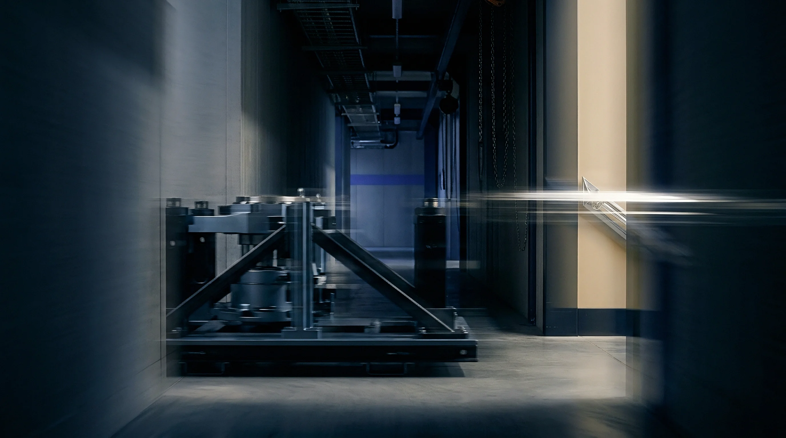 Heavy steel structural assembly rests on a wheeled transport cart inside a dim industrial facility corridor.